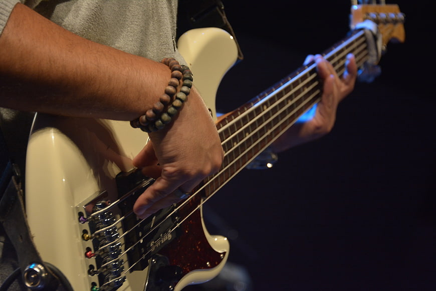 Close-up of musician playing white electric bass guitar on stage