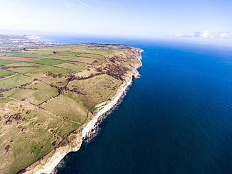 Aerial view of white cliffs and green coastal fields meeting the blue ocean