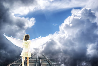Woman with angel wings standing on railway tracks under dramatic clouds