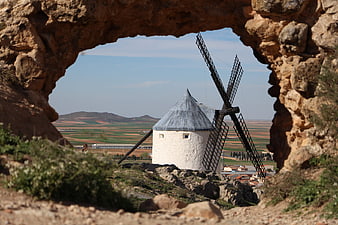 Traditional white windmill framed by stone archway in rural landscape