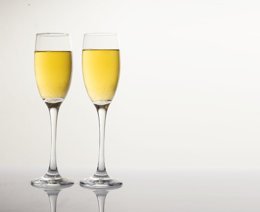 Two Champagne Flutes with Golden Bubbles on White Background