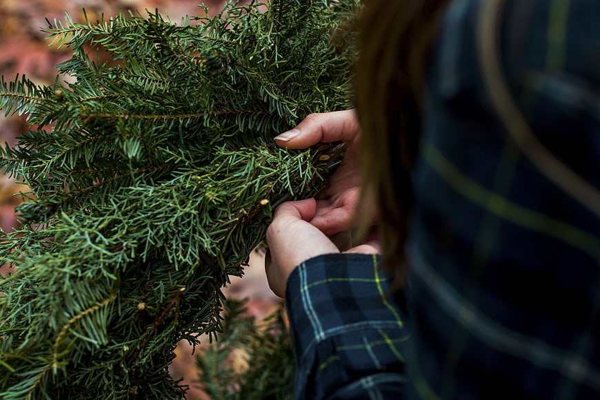 Close-up of hands arranging evergreen branches for wreath