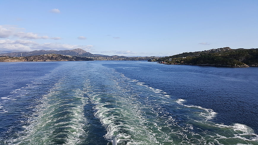 Boat wake trailing behind ship in Norwegian fjord landscape