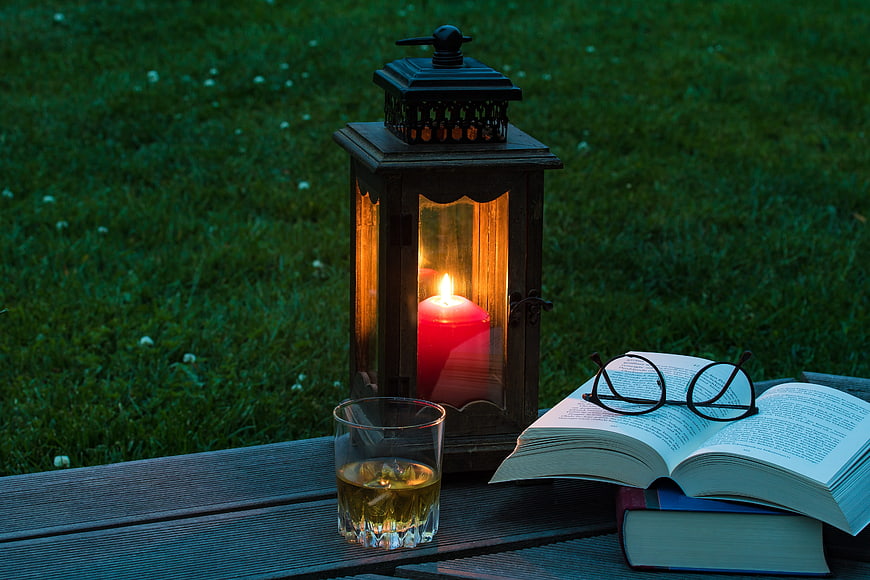 Relaxing evening reading setup with lantern, whiskey, and books