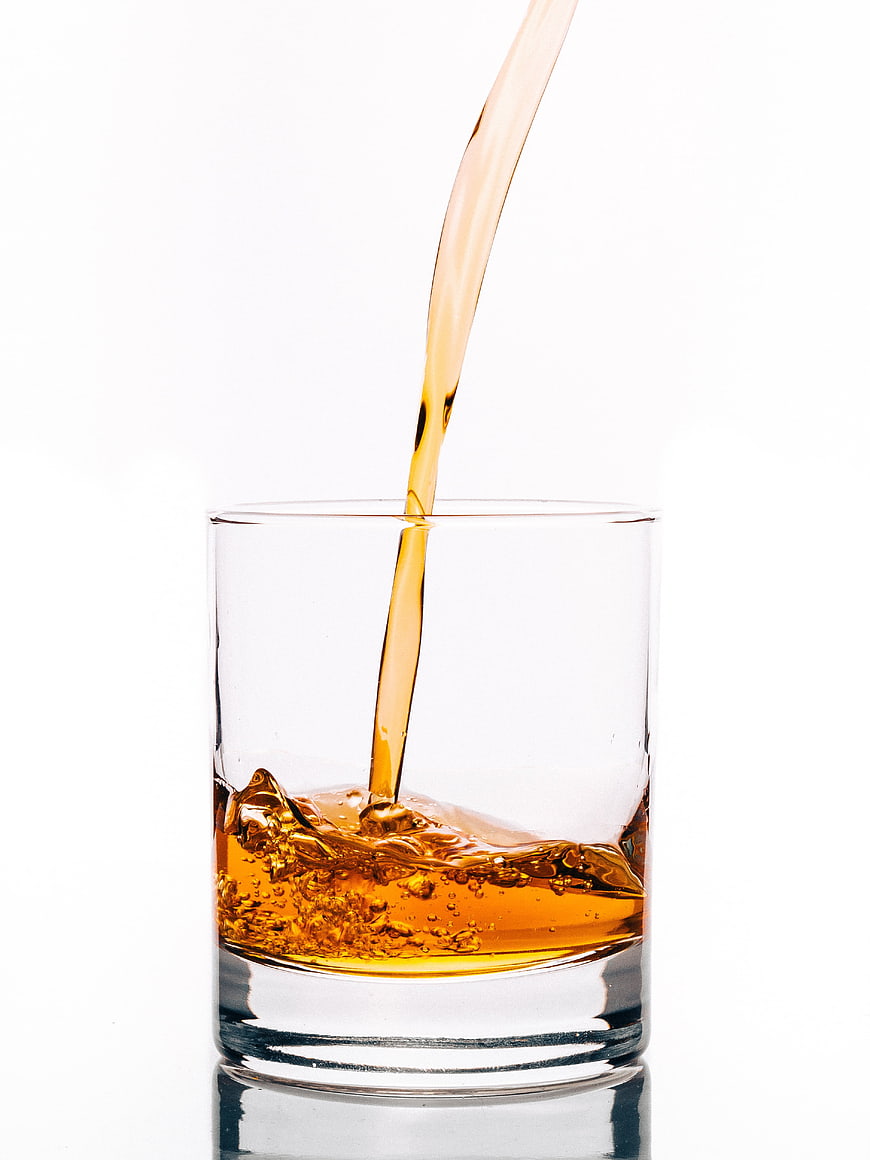 Amber Whisky Pouring Into Clear Glass Tumbler On White Background