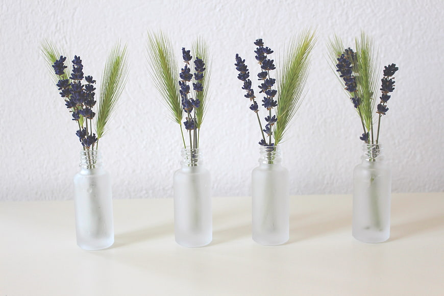 Four frosted glass vases with lavender and wheat on a white background