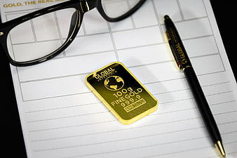 Gold bar, pen, and glasses on financial document