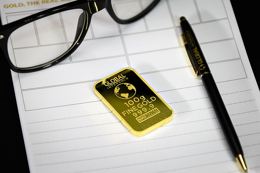 Gold bar, pen, and glasses on financial document