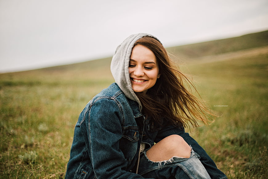 Smiling young woman in denim jacket sitting in grassy field