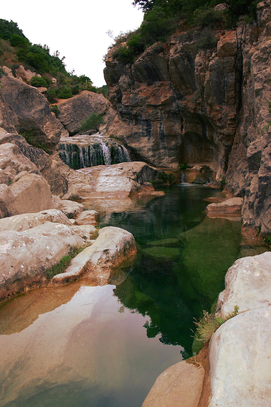 Serene natural waterfall cascading into a deep green pool in rocky canyon