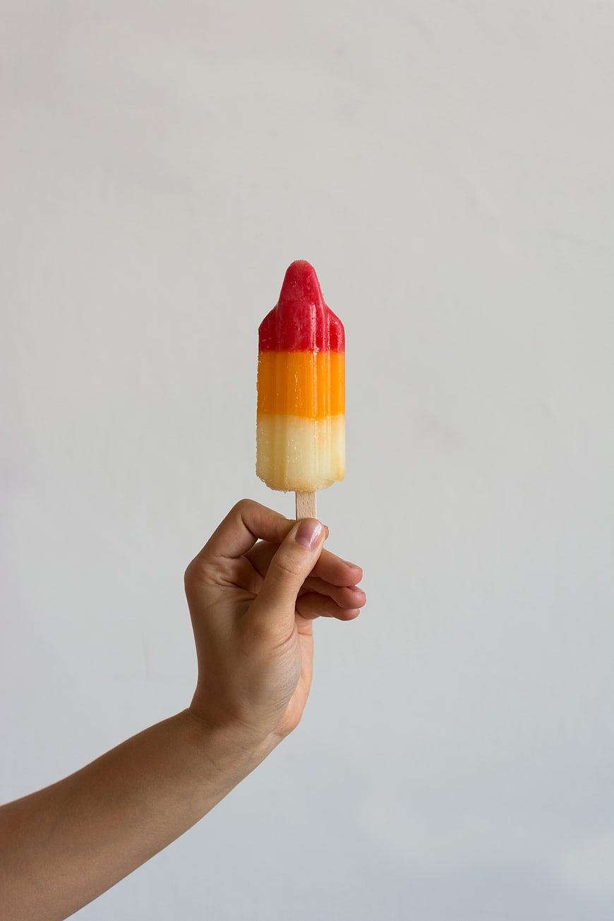 Hand Holding Tri-Color Rocket Popsicle on White Background