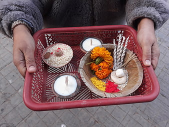 Hands holding Hindu puja tray with marigolds and ghee lamps