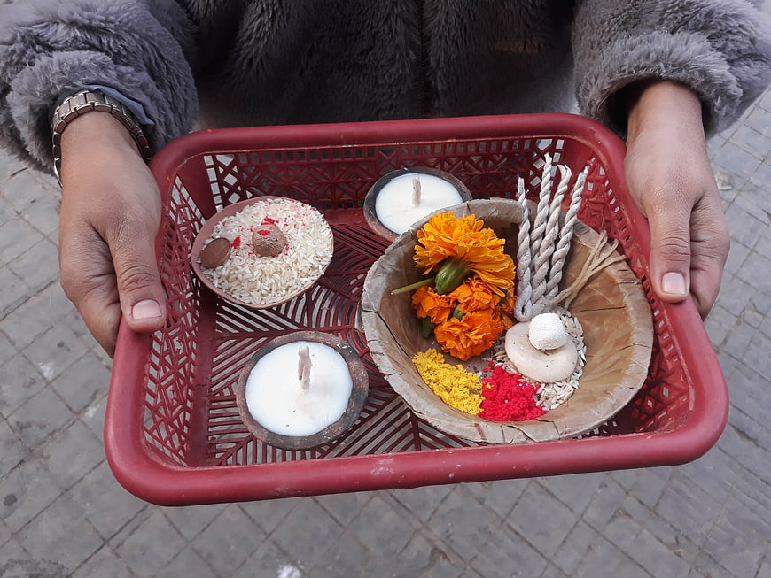 Hands holding Hindu puja tray with marigolds and ghee lamps