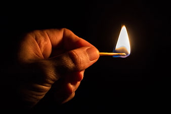 Hand Holding Lit Matchstick in Darkness