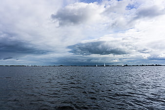 Sailboats on a wide river under a dramatic cloudy sky