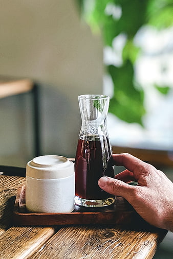 Hand holding glass carafe of cold brew coffee on wooden tray