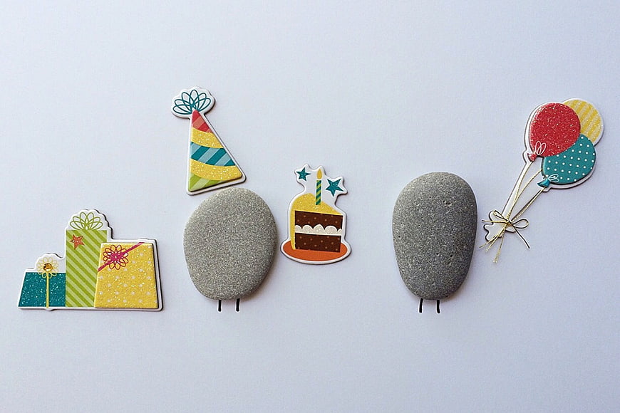 Cute stone characters with birthday party accessories flat lay