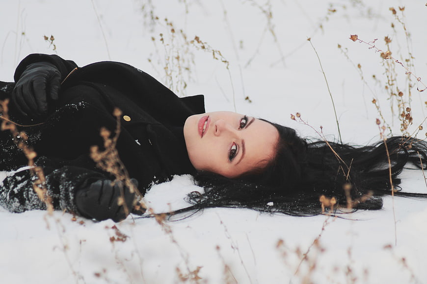 Woman lying in snow with dried plants