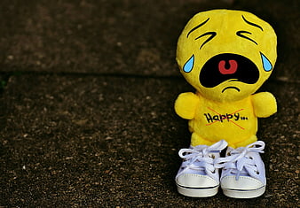 Sad yellow plush toy with sneakers on dark textured ground