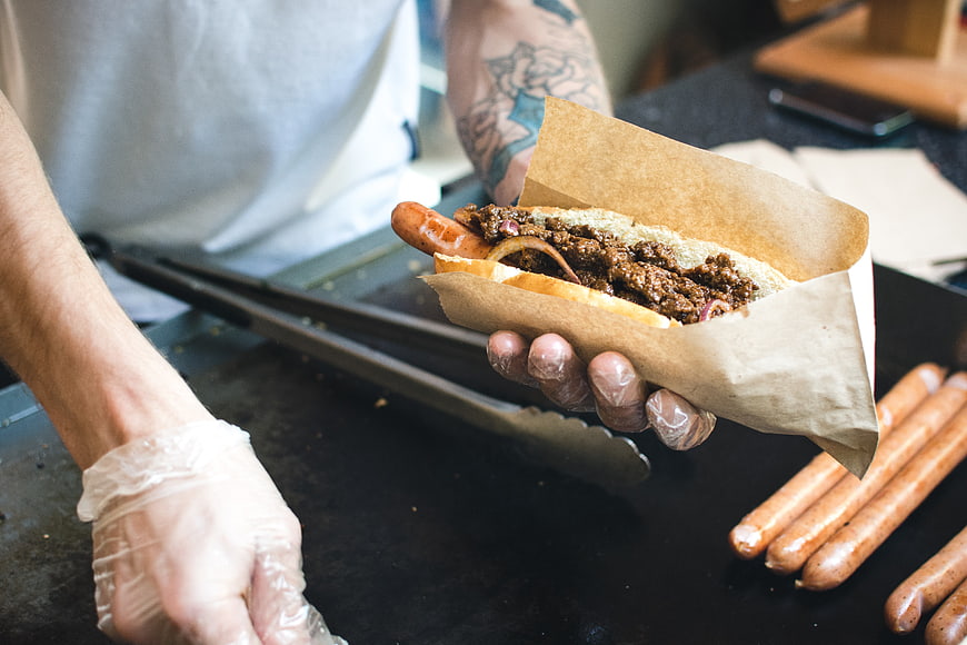Chef holding loaded chili cheese hot dog on griddle