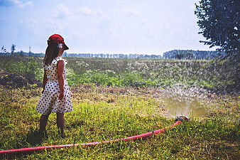 Little Girl Watching Sprinkler in Green Field