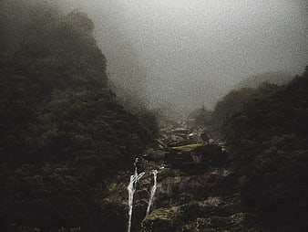 Misty waterfall cascading through dark forested mountain valley
