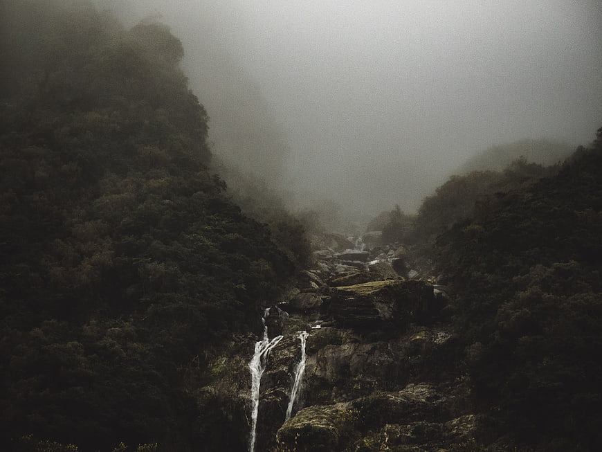 Misty waterfall cascading through dark forested mountain valley
