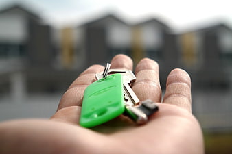 Hand Holding House Keys with Blurred New Homes Background