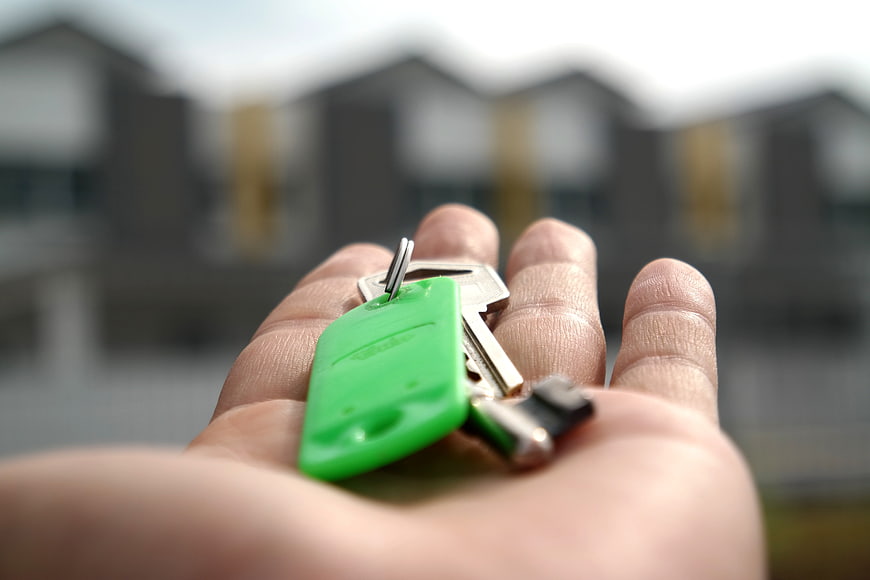 Hand Holding House Keys with Blurred New Homes Background