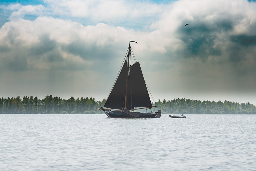 Traditional Sailboat on Lake with Forest Background