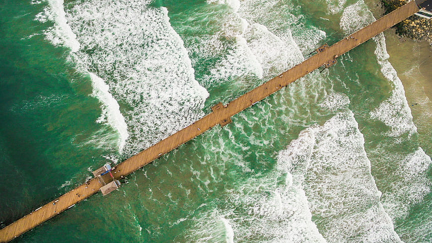 Aerial View of Wooden Pier Extending into Green Ocean Waves