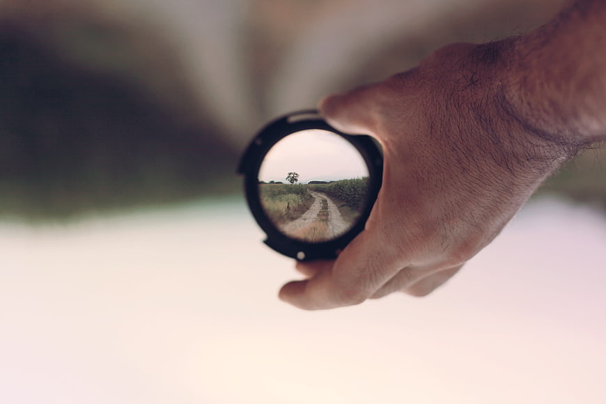 Hand holding camera lens cap with landscape reflection