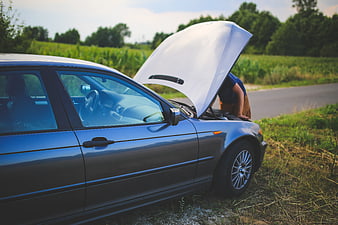 Man inspecting engine of broken down car on roadside