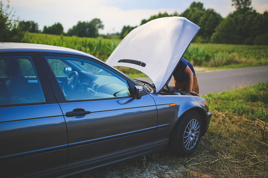 Man inspecting engine of broken down car on roadside