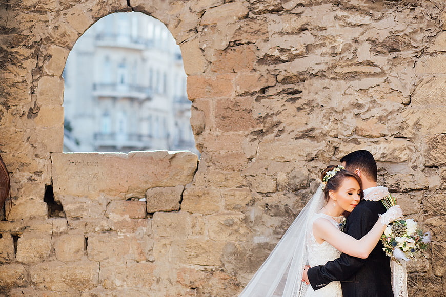 Bride and Groom Hugging by Ancient Stone Wall