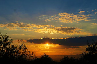 Dramatic sunset with sun rays through clouds over silhouetted landscape