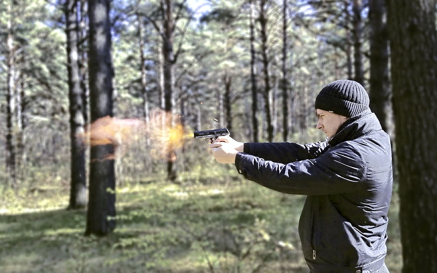 Man Shooting Pistol With Muzzle Flash In Pine Forest