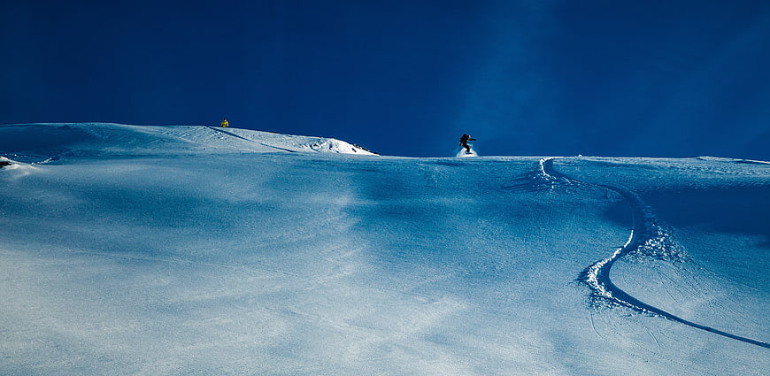 Snowboarder carving fresh powder on a vast blue mountain slope