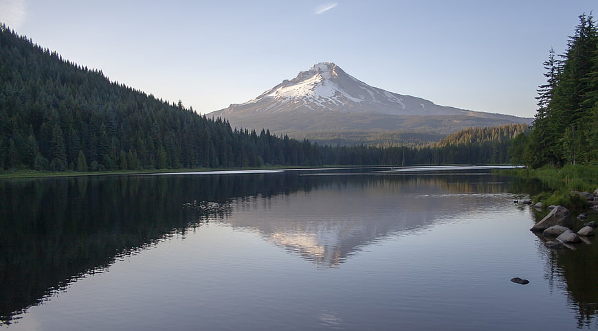 Snow-capped mountain reflected in calm lake surrounded by forest