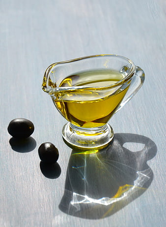 Glass gravy boat with olive oil and black olives on a light blue surface