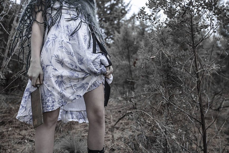 Woman holding cleaver in desaturated forest horror concept