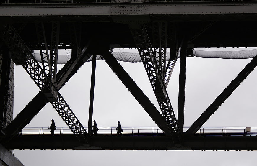 Silhouettes of Pedestrians Walking Under Steel Bridge Structure