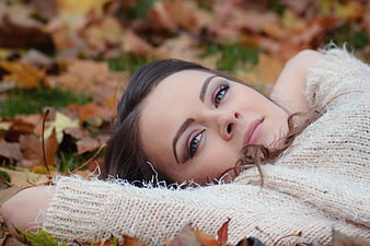 Young woman lying in autumn leaves wearing beige sweater