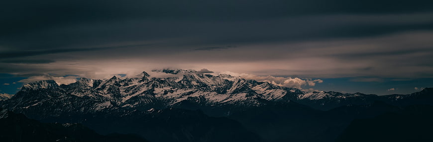 Dramatic Snow-Capped Mountain Range Under Dark Stormy Sky