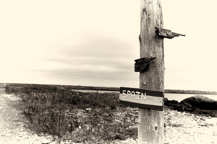 Sepia wooden signpost pointing to Spain on a rocky coast