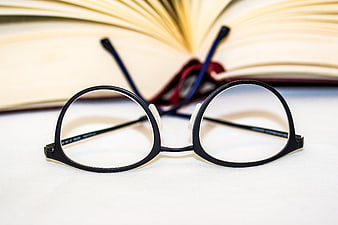 Black Reading Glasses on White Surface with Open Book