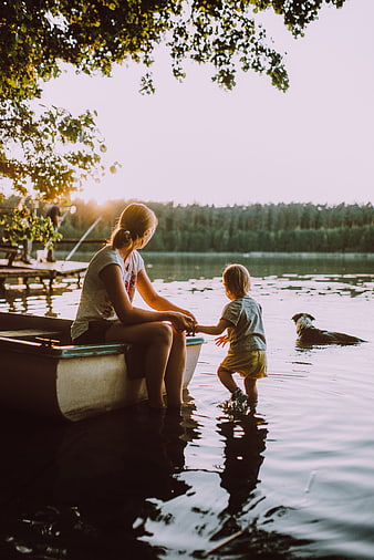Mother and child holding hands by a lake with a dog