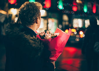 Man holding bouquet of roses on city street at night