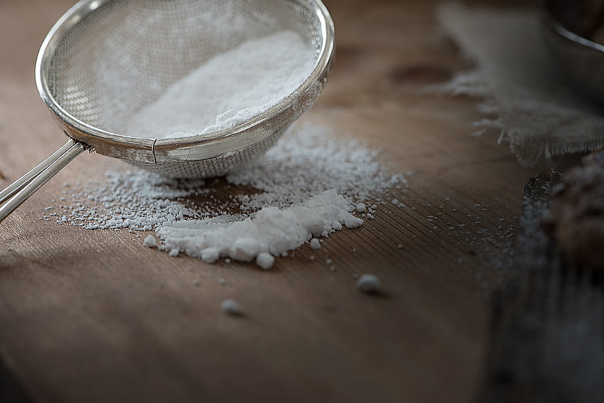 Metal sieve with powdered sugar on rustic wooden table