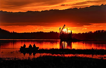 Silhouetted fishermen in a boat on a lake at sunset
